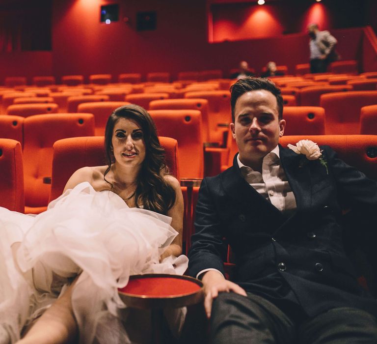 Bride and groom sat in the cinema wearing their wedding outfits