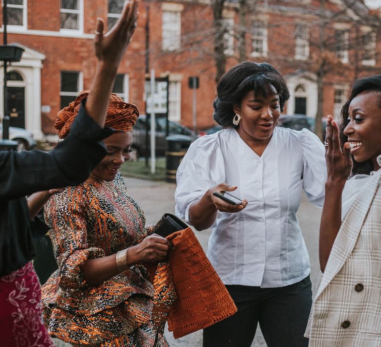 Laughing bride in grey checked jacket stands with smiling guests outside Bridge Community Church wedding