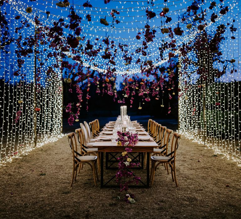 Suspended floral installation and fairy light canopy over rustic wooden wedding table at enchanted forest wedding in Italy