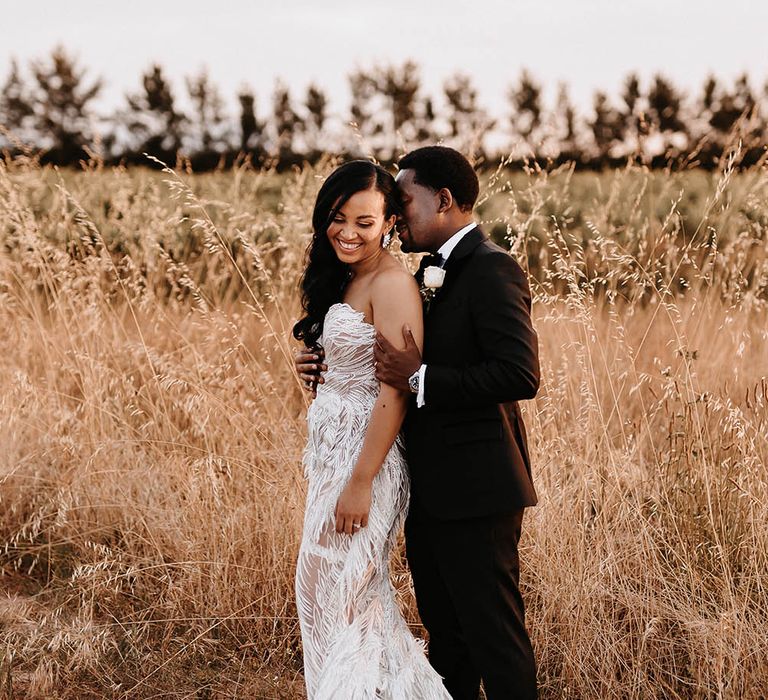 Groom in a black-tie suit kissing his bride's neck in a Biji La Maison de Couture wedding dress