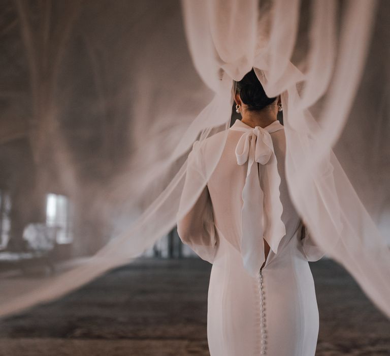 Brides veil blows around her and shows off the back of her buttoned gown