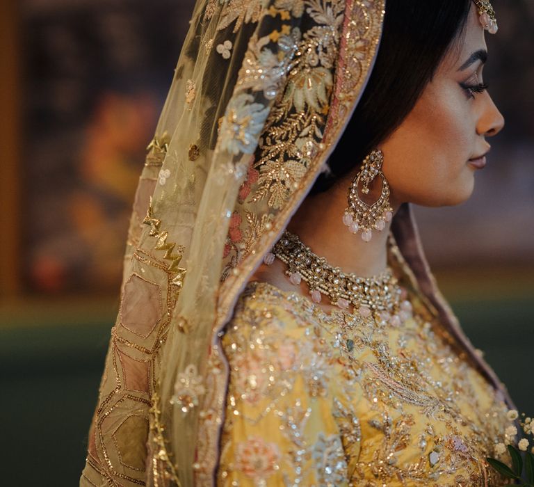 Beautiful Bengali bride in a pastel saree and veil wearing a gold necklace and earrings