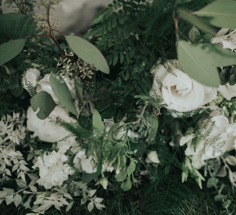 Close up if white and green wedding bouquet with white roses, olive leaves and green ferns.