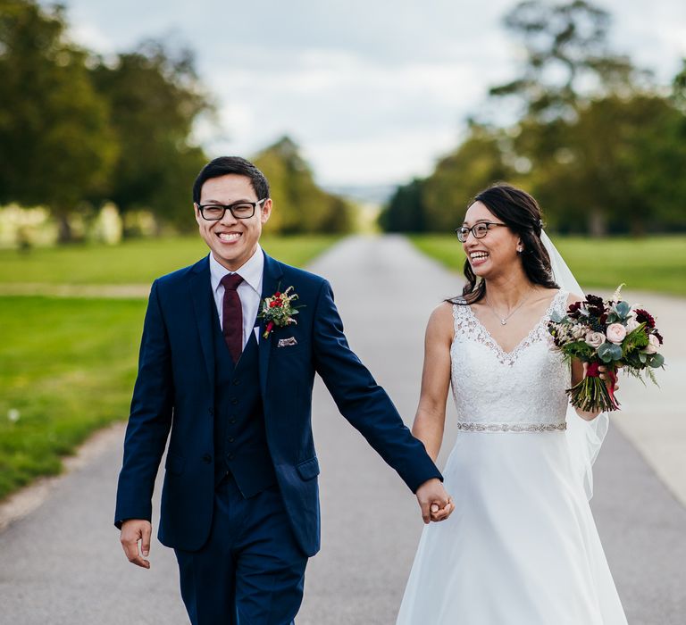 Bride & groom walk hand in hand as bride carries floral bouquet