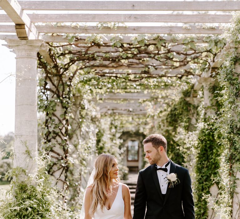 Bride & groom walk beneath pergola