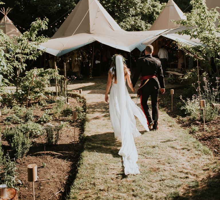 Boho bride in a floaty dress with feather headdresses and groom in military uniform for outdoor tipi wedding 