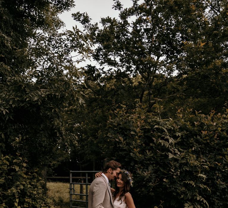 Bride & groom stand on wooden bridge as groom leans in to bride as she wraps her arm around him