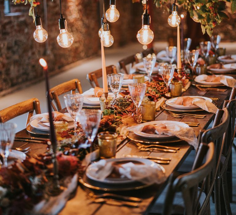 Pumpkin spice wedding tablescape with tapered candles, foliage centrepiece gold rimmed glassware and hanging Edison bulbs