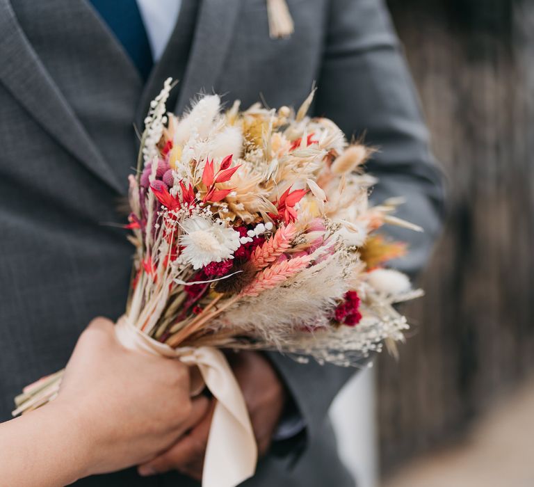 Bride holds dried floral bouquet complete in vibrant colours and tied with white silk ribbon