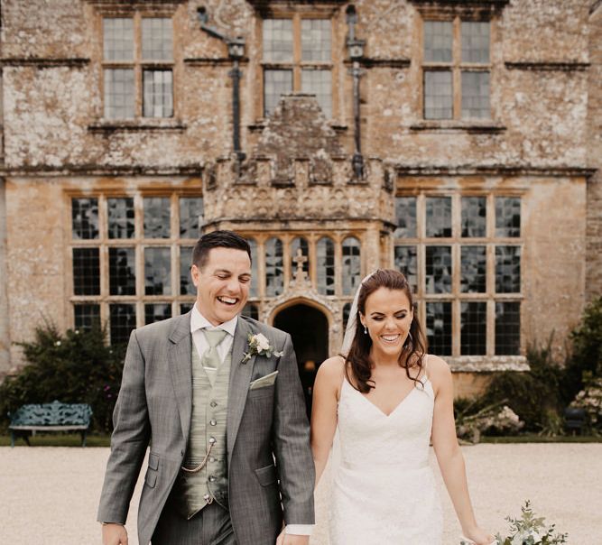 Groom in a grey wedding suit with silk waistcoat and cravat holding hands with his bride 