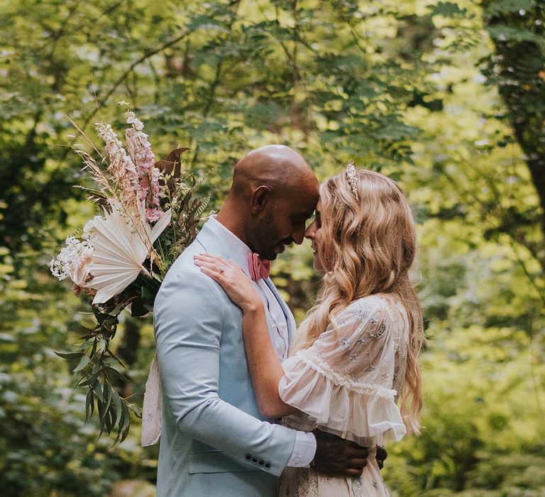 Bride & groom lean in to kiss one another surrounded by green trees 