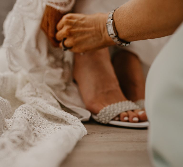 Bride has her wedding shoes done up by guest on her wedding day as she gets ready | Mark Bamforth Photography