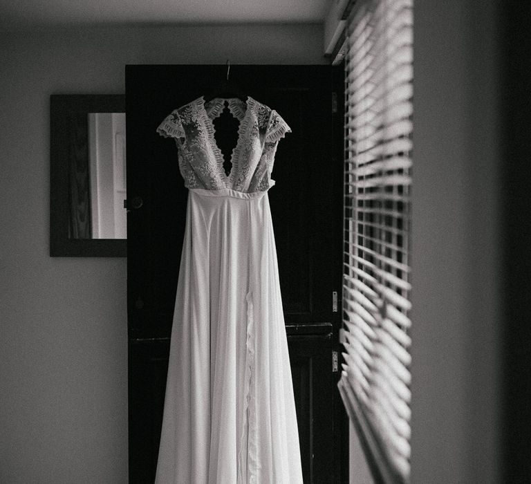 White lace cap sleeve wedding dress with open back hanging on door before late summer wedding with woodland wedding ceremony 