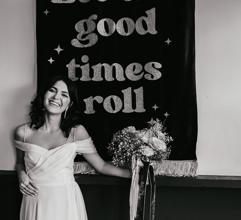 Bride in a cold shoulder wedding dress standing next to a let the good times roll wedding banner 