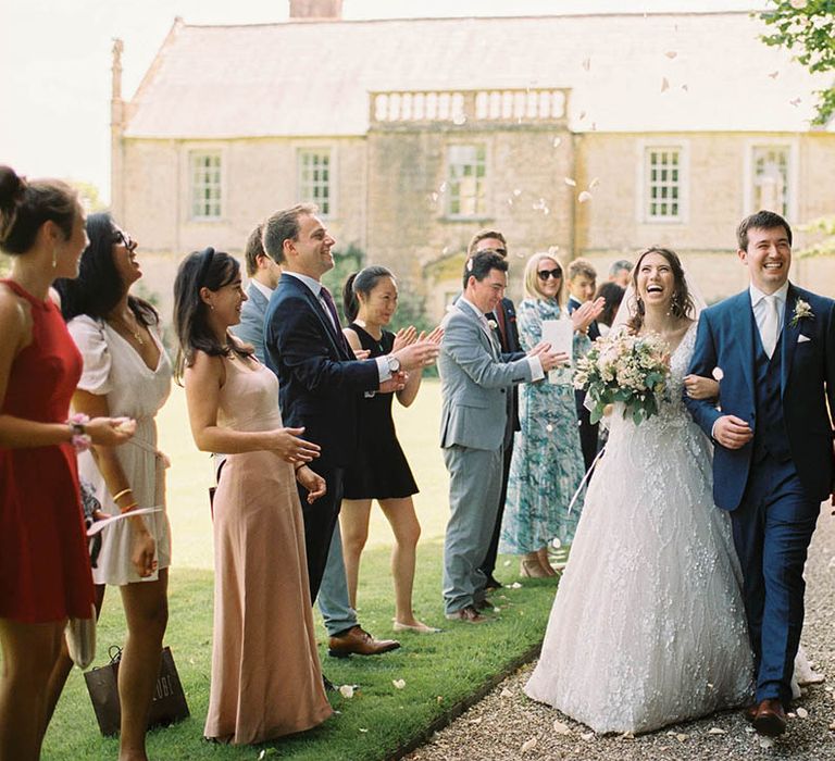 Bride & groom walk arm in arm through wedding guests who through confetti 