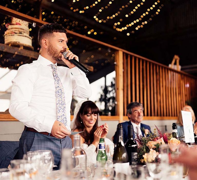 Groom in blue check trousers and a floral tie giving his wedding speech at Stone Barn Cotswolds wedding venue 