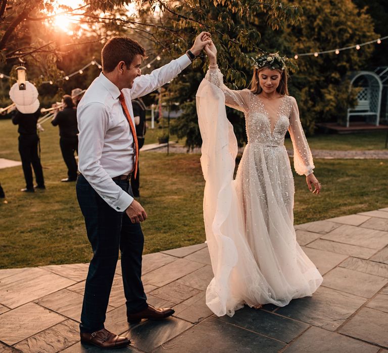 Bride in embroidered Julie Vino wedding dress and flower crown dances at golden hour with groom in white shirt at outdoor wedding reception 