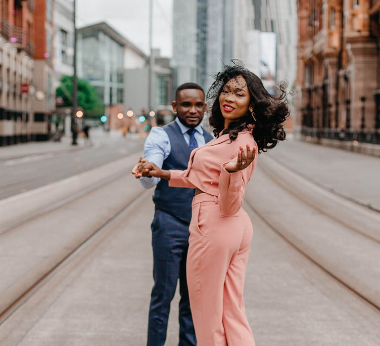 Bride wears pale pink suit complete with black birdcage headpiece 