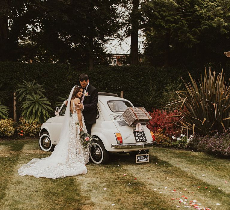 Bride & groom stand on lawn next to their restored Fiat 500 wedding car