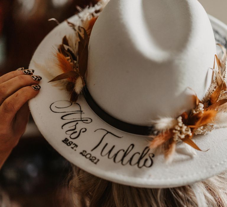 Bride holds white personalised fedora from Rebecca Anne Designs that reads 'Mrs Tudds' decorated with dried flowers