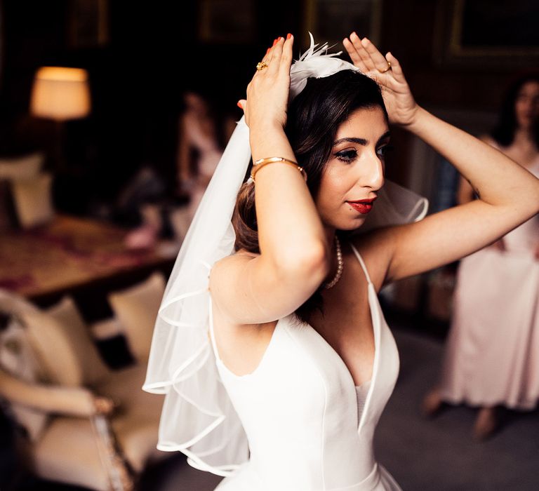 Bridesmaid in wedding dress with plunging neckline adjusts her veil as she gets ready before wedding