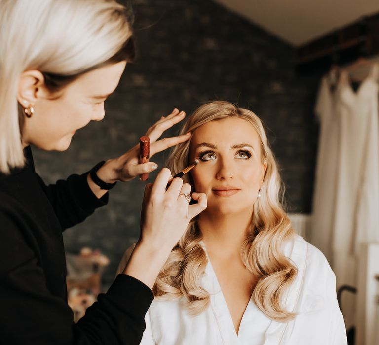 Bride with blonde curled hair has her makeup done before wedding