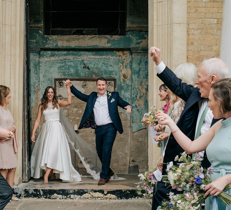 Bride and groom walk through wedding guests as a married couple with bride wearing long lace detailed veil 