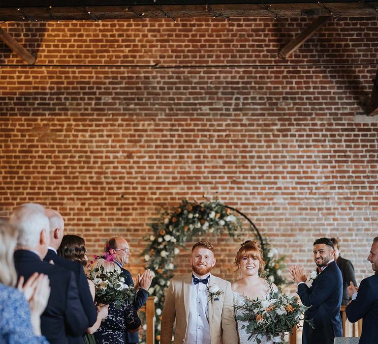 Bride and groom walk back down the aisle as a married couple with bride in lace Maggie Sottero dress 