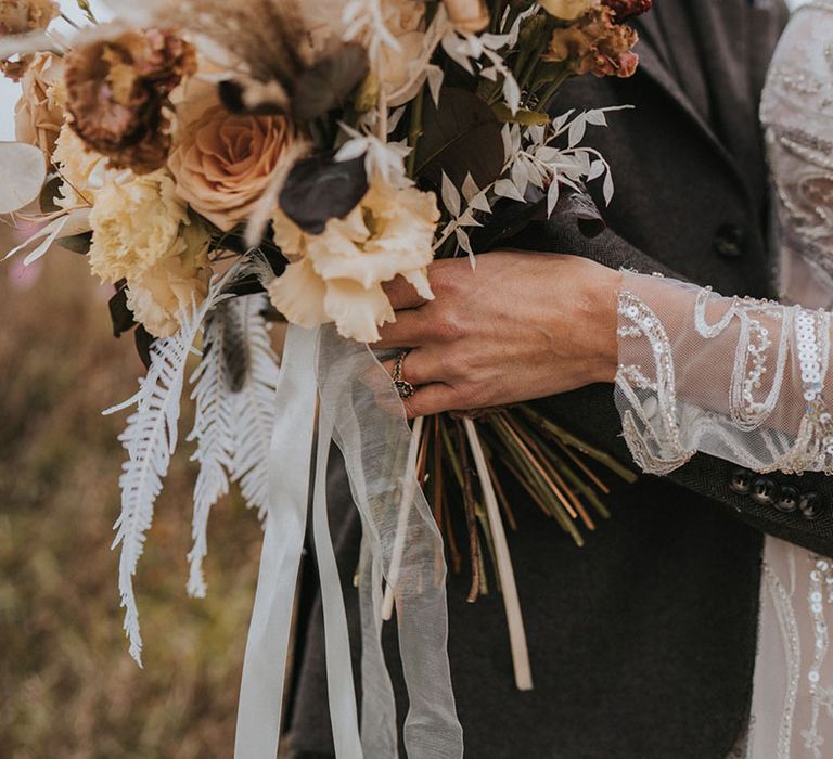 Bride in Zavana Couture wedding dress hugs with groom in dark grey suit ith wedding bouquet tied with whnite ribbon