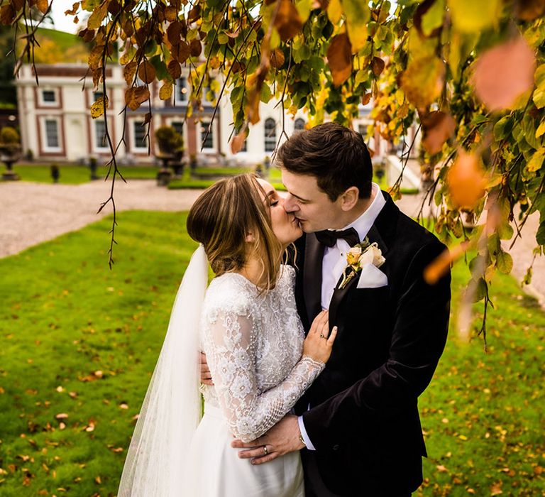 Bride and groom share a kiss under autumnal leaves for autumn wedding at country house