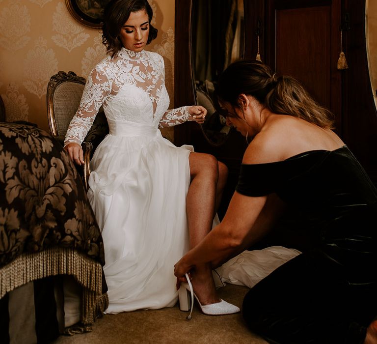 Bridesmaid helps the bride into her Charlotte Mills wedding shoes in illusion lace wedding dress 