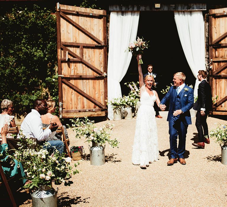 Bride and groom exit their ceremony as a married couple with vintage milk turns full of flowers as decor 