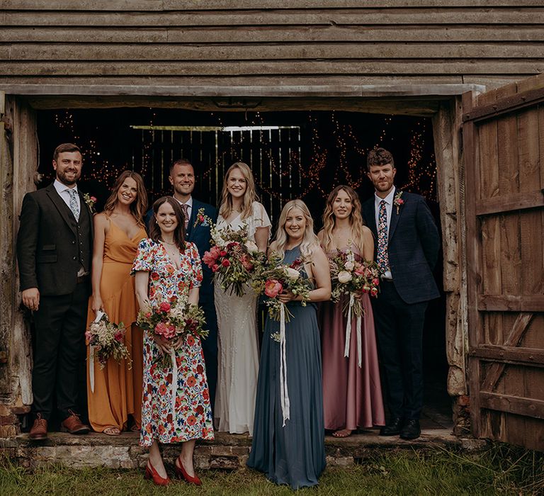 Wedding party with groomsmen and bridesmaids in mismatching colour and style outfits for relaxed rustic barn wedding 