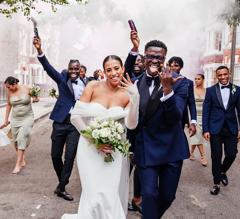 Bride shows off her ring as the wedding party release smoke bombs and celebrate together with bridesmaids in mint green satin dresses and groomsmen in black tie