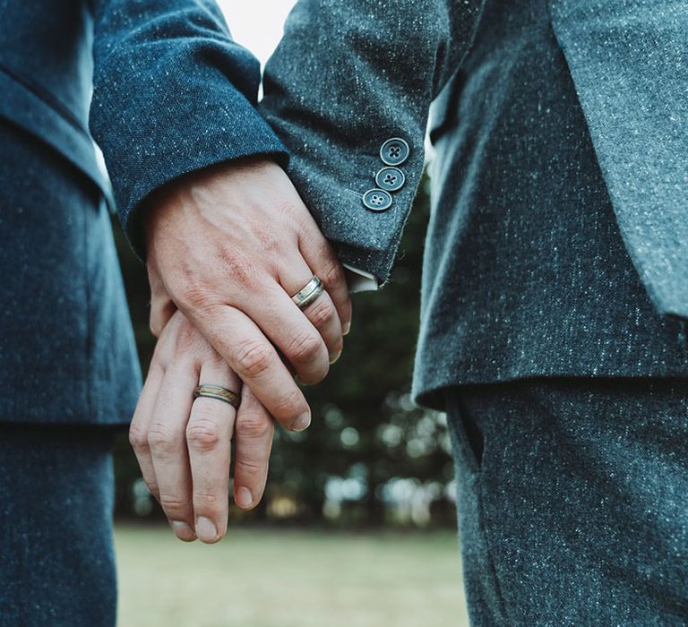 Grooms hold hands showing off their wood inlaid in titanium wedding bands