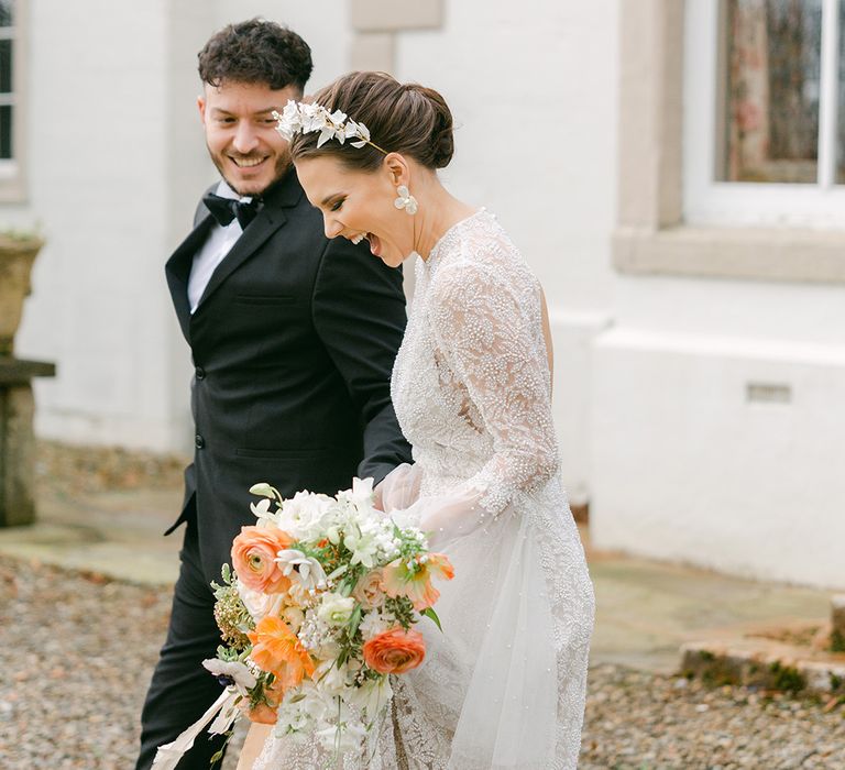 Bride in a beaded wedding dress holding a peach and white wedding bouquet with a chic up do and bridal headdress 