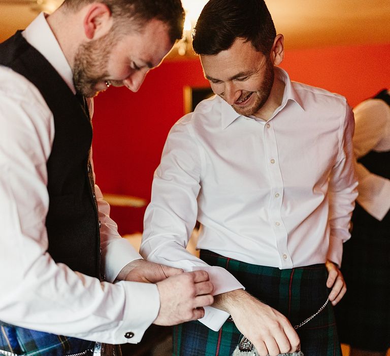 Groomsmen helps groom put on cufflinks on the morning of his wedding day 