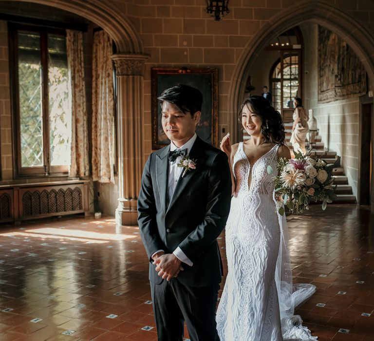 Bride wearing embellished lace Viero wedding dress comes behind her groom wearing black-tie during first look moment at La Baronia in Barcelona