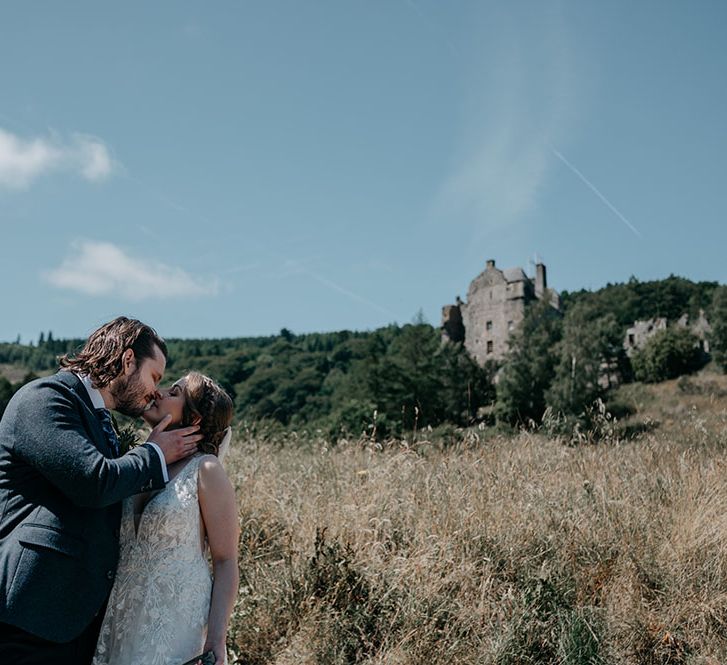 Bride & groom kiss in front of Neidpath Castle surrounded by greenery in Scotland 