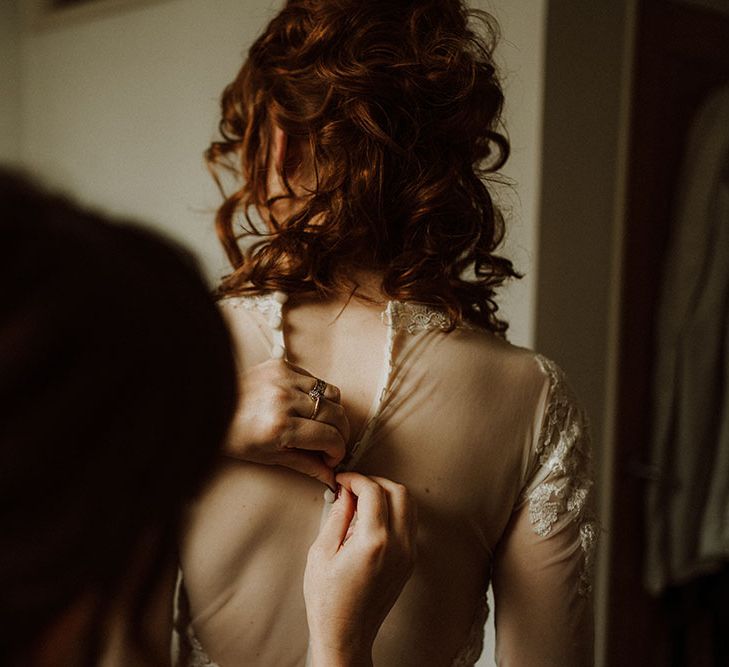 Bride has the back of her sheer lace dress buttoned 