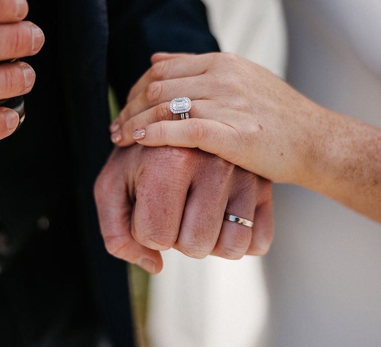 Bride with abstract pattern wedding nails with a large diamond emerald cut engagement ring holding hands with the groom with a plain silver wedding band 