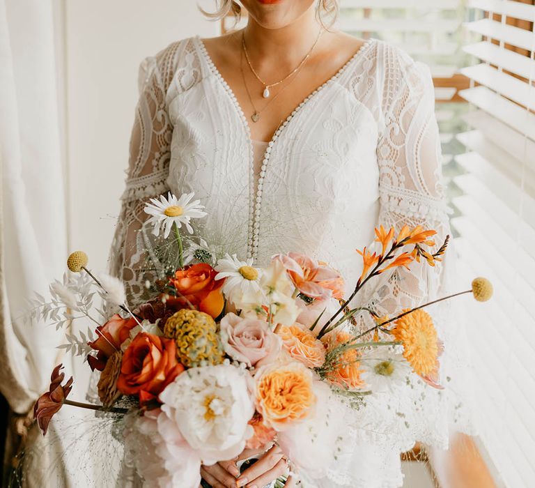 Smiling bride in a boho lace wedding dress with orange, pink and white wedding bouquet for her retro wedding 