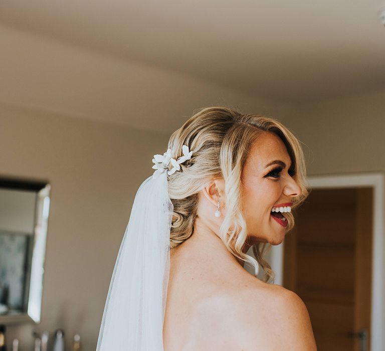 Bride with curled blonde hair in an updo with pearl earrings and white flower hair accessory