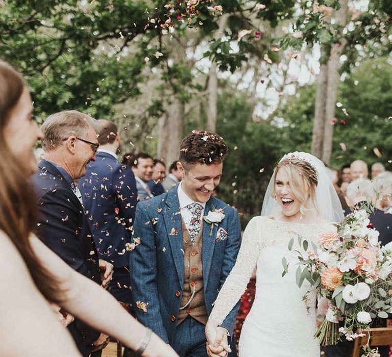 Bride in long sleeve wedding dress with groom in a three piece blue suit with a flower tie and handkerchief 