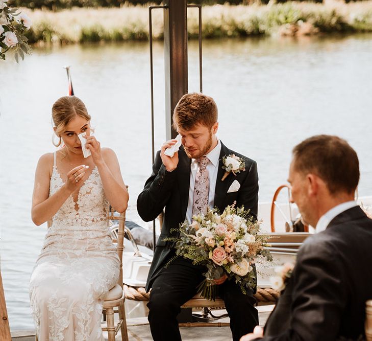 Emotional bride & groom sit in front of the Thames during humanist wedding ceremony