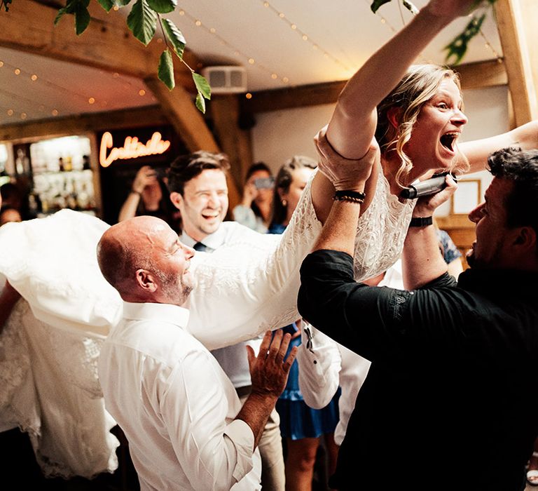 Wedding guests lift up the bride as they dance together at the wedding reception 