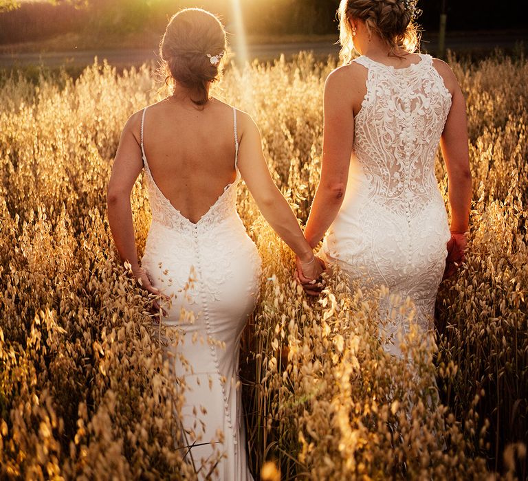 Brides walk together holding hands as the sun sets for their summer wedding 