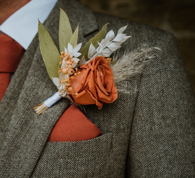 Groom in grey suit with matching orange tie, pocket square, and rose boutonniere with dried flowers