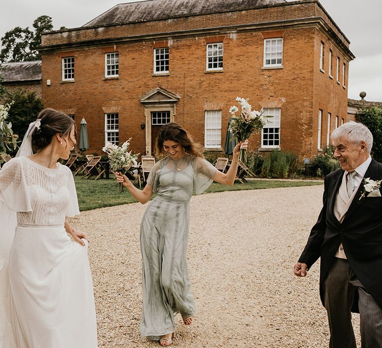 Bride in batwing sleeve and polka dot detail wedding dress dancing with bridesmaid in mint green bridesmaid dress, both holding neutral toned bouquets