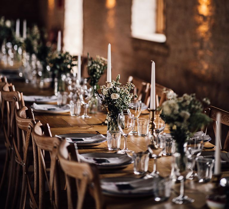 Classic wedding tablescape with white candles in gold candleholders with small arrangements of white flowers 